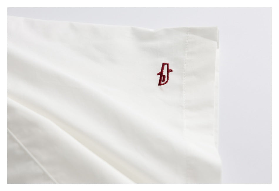 Close-up of a red embroidered emblem on the cuff of a white shirt.