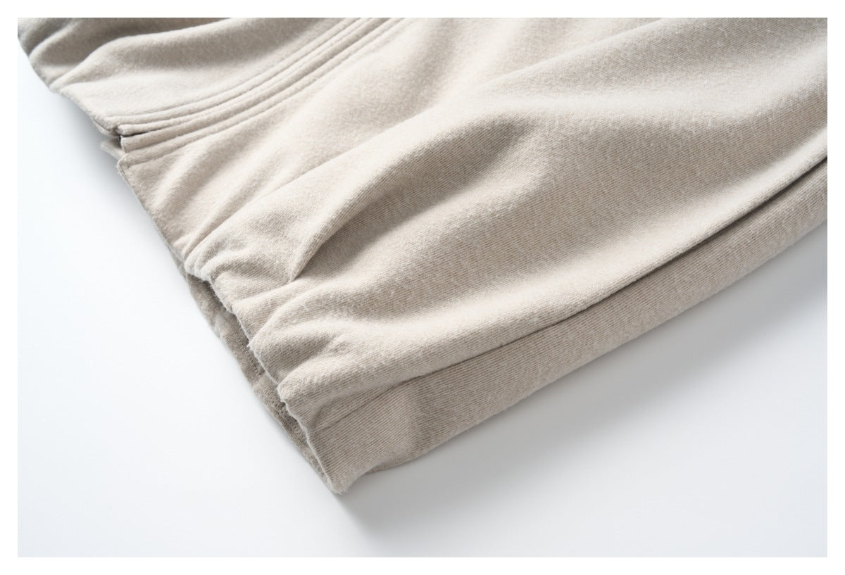 Close-up of gathered stitching and a folded edge on beige heathered fabric.