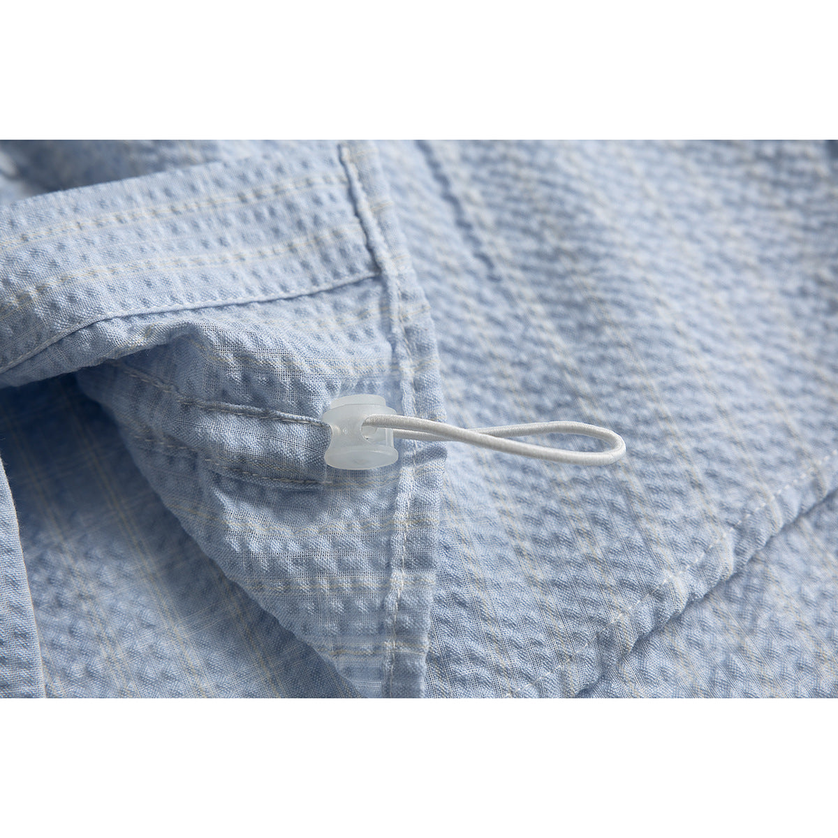 Close-up of a small white loop fastener attached to the pale blue textured shirt.