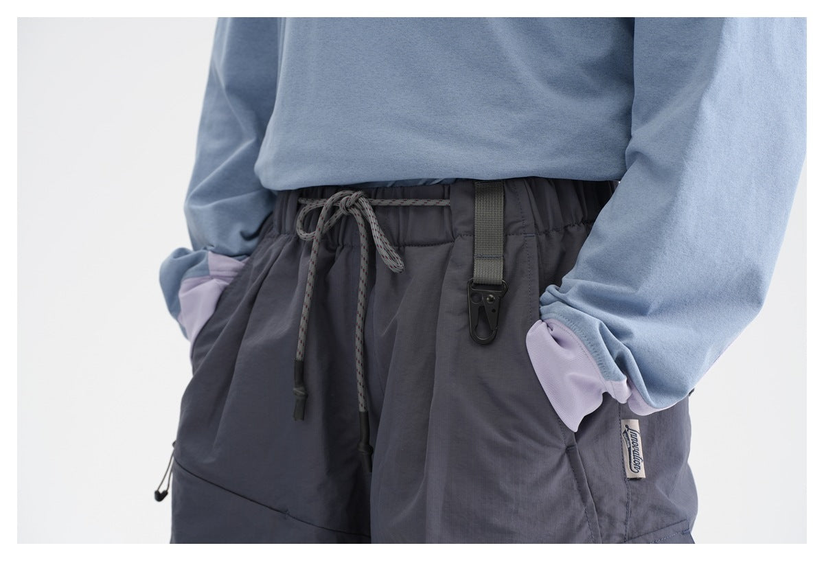 Close-up of dark gray cargo pants with a drawstring waist, hanging clip, and lavender pocket accents, worn with a blue top.