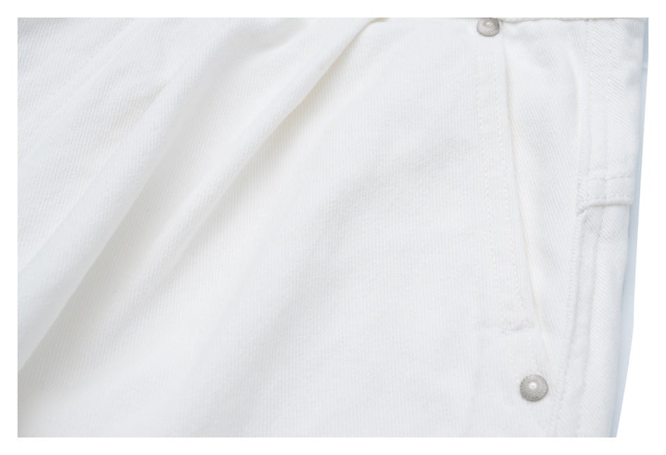 Close-up of white trousers showing a seam, a narrow pocket edge and two silver rivet buttons.