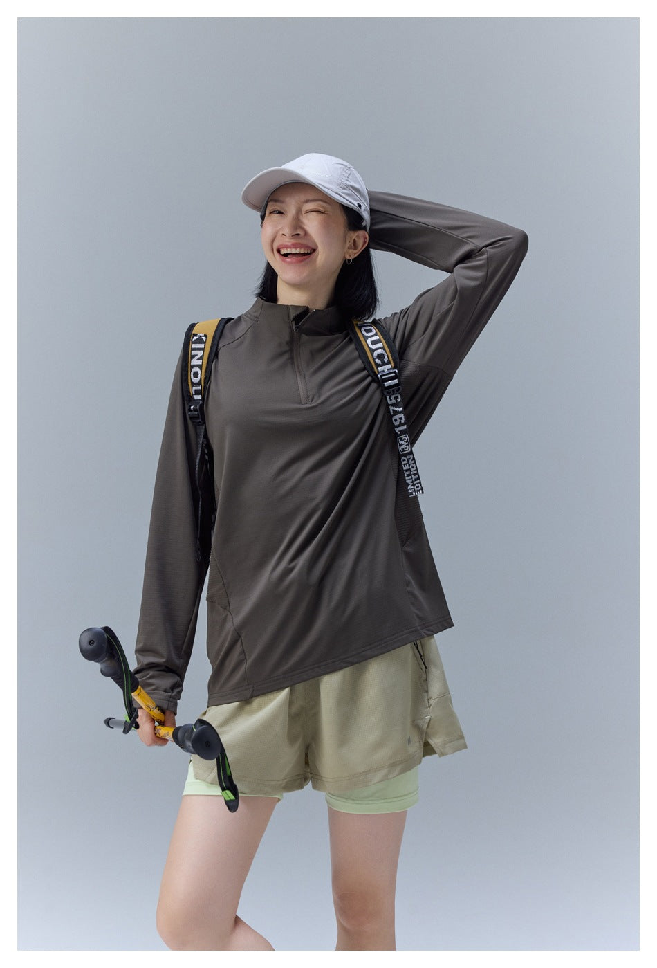 Closer view of a model wearing a dark taupe quarter-zip top and khaki shorts with a hiking backpack.