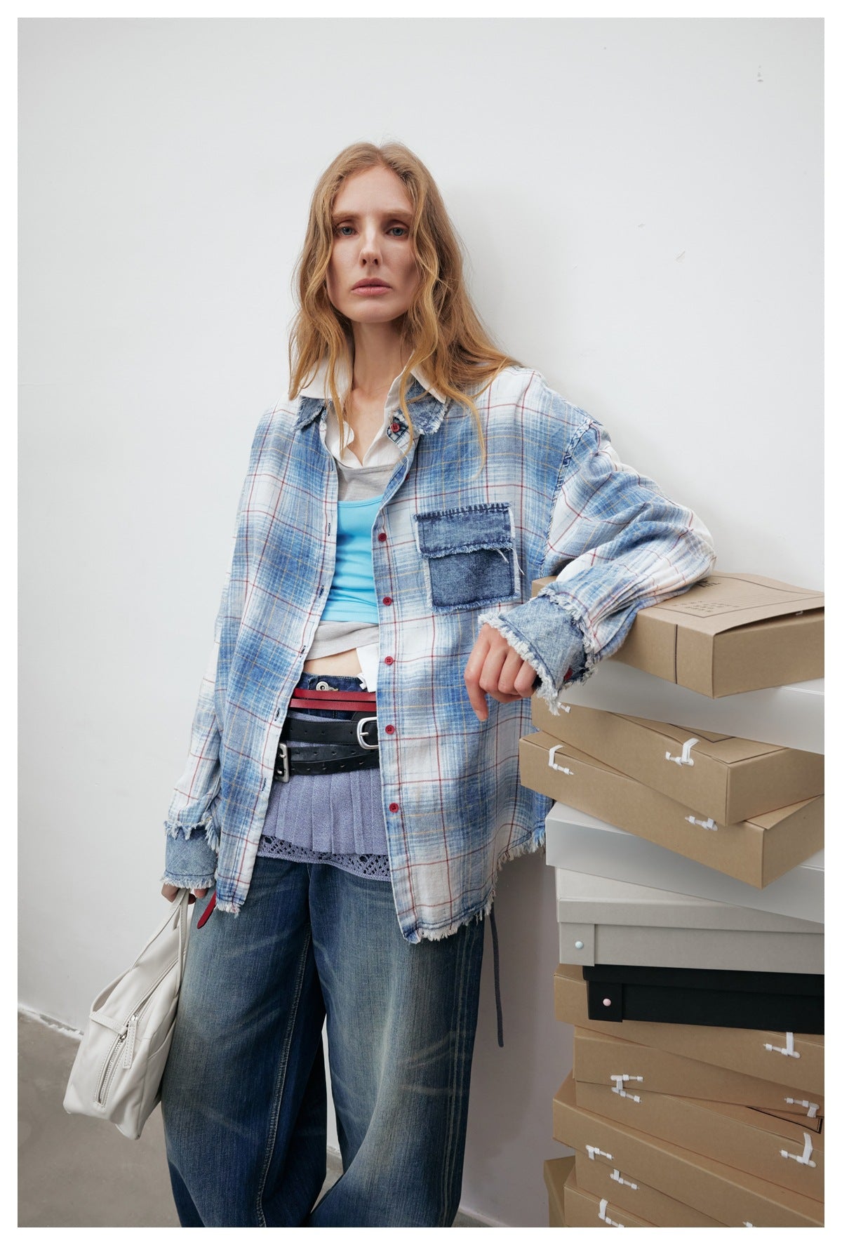 Model wearing a blue-and-white plaid shirt with red and yellow lines, dark denim patch pocket, red buttons and frayed edges.