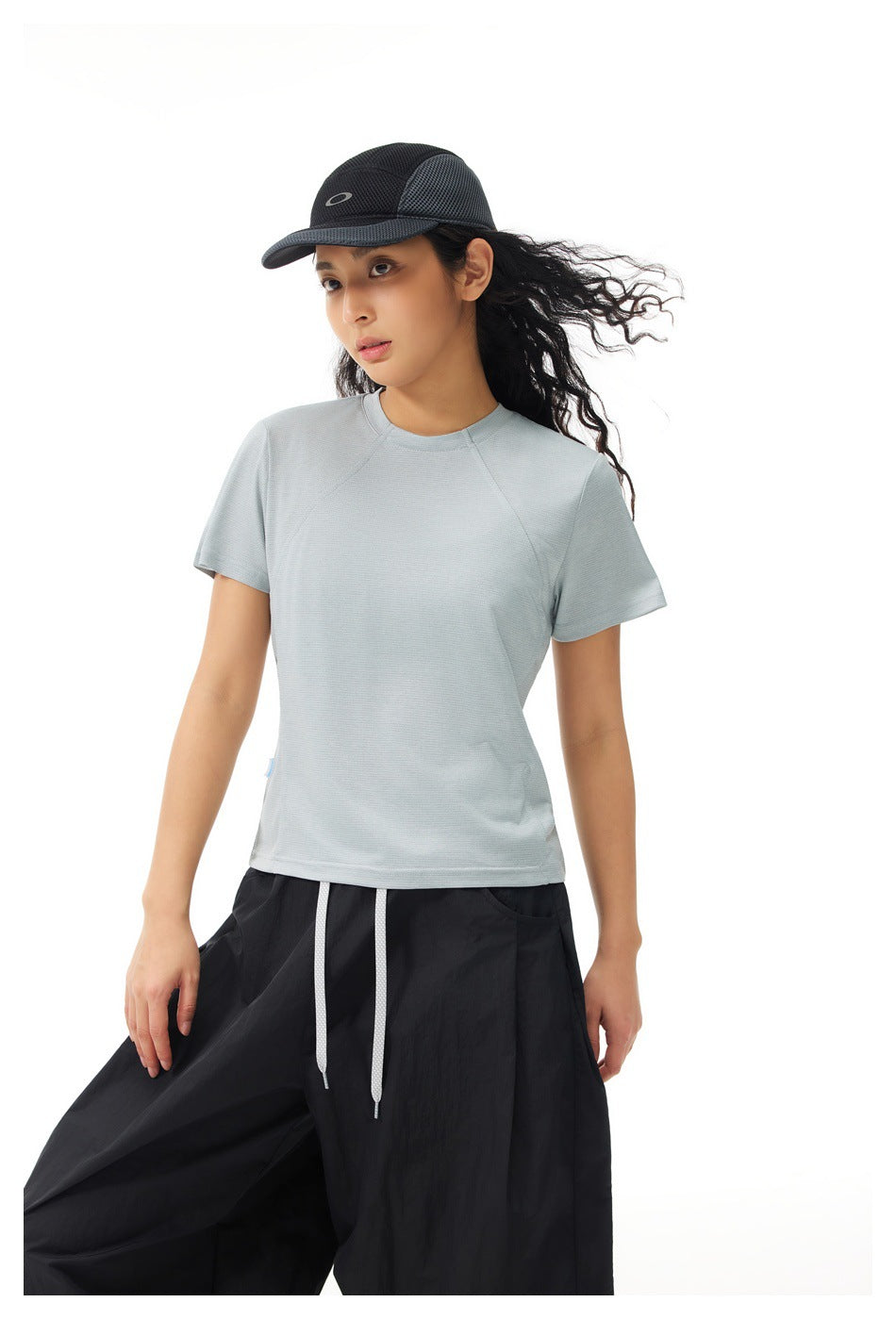 Model wearing a pale gray short-sleeve shirt with raglan seams and black wide-leg pants, shown from the front.