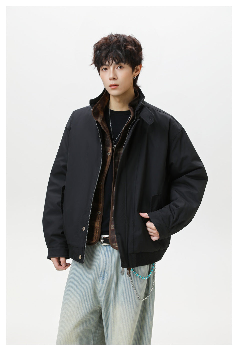 Model in black zip jacket with plaid inner layer, one hand in pocket, with striped pants and bead chain
