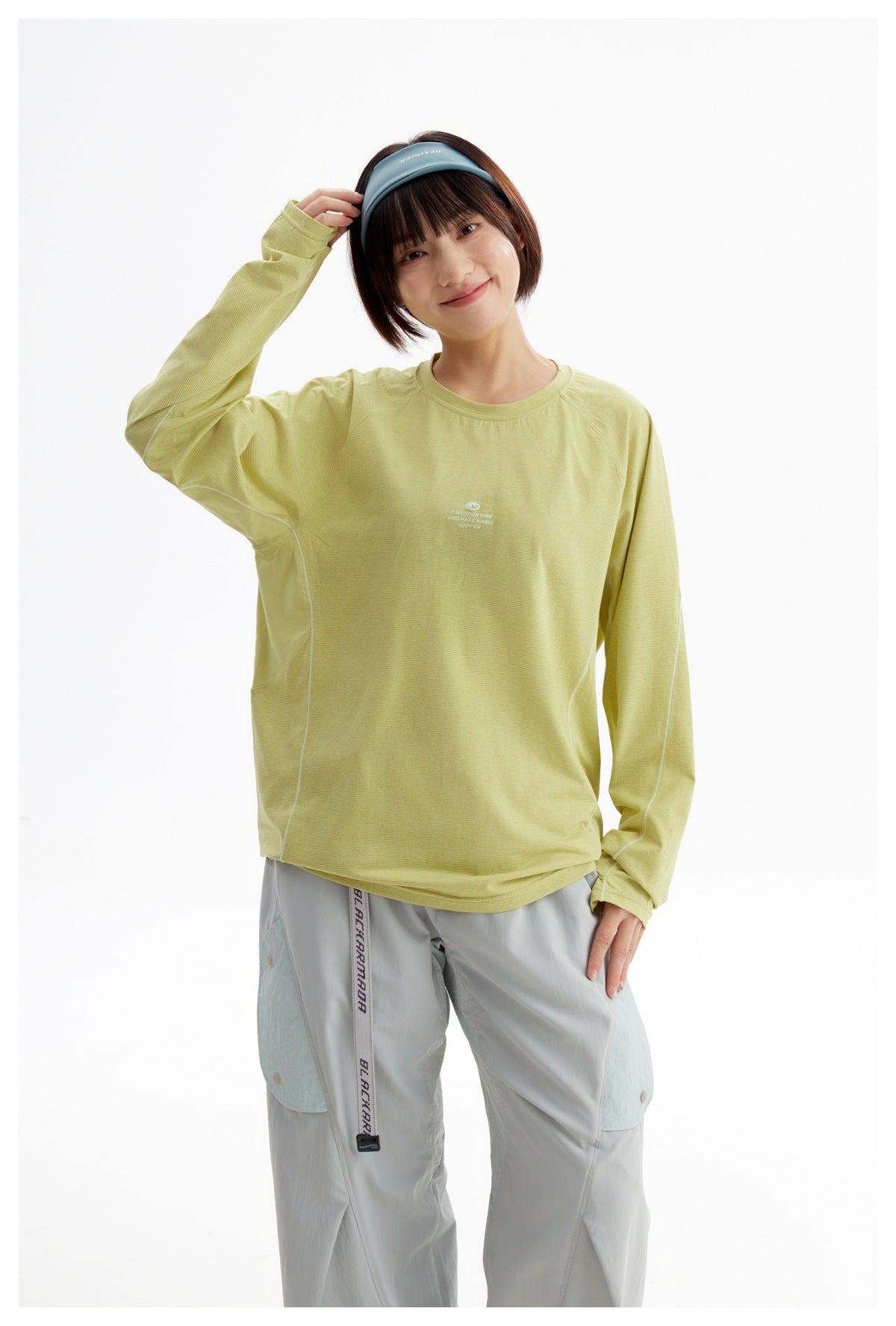 Model wearing a pale yellow-green long-sleeve top with subtle chest print and light gray pants, shown from the front.
