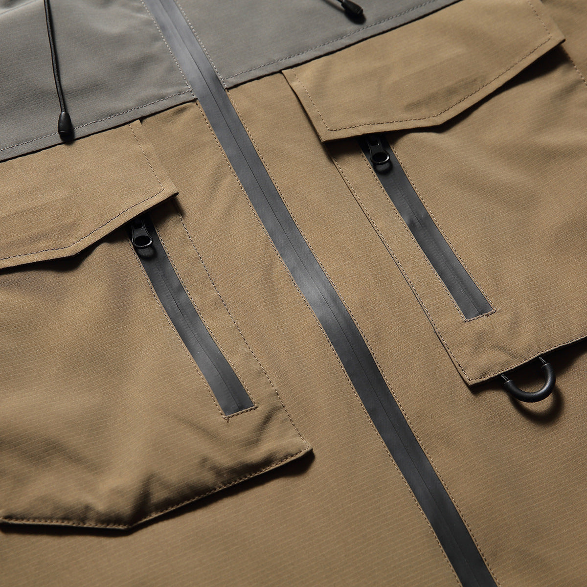 Close-up of tan jacket panels with flap pockets, black vertical zippers and a center front zipper.