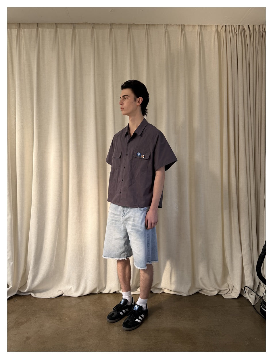 Model in dark gray short-sleeve shirt with chest pockets, light wash denim shorts and black sneakers, side view