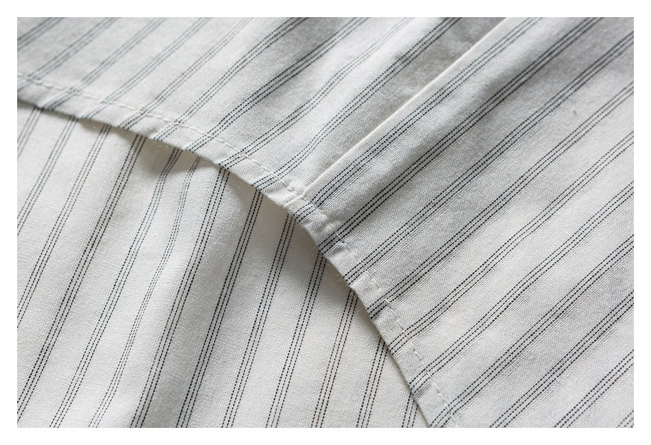 Close-up of light gray fabric with narrow dark pinstripes and a curved stitched edge.