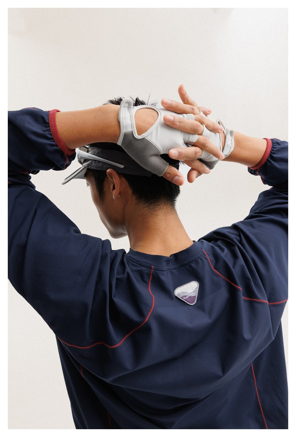 Rear view of a model wearing a navy long-sleeve athletic top with red seam accents, gray gloves and a visor.