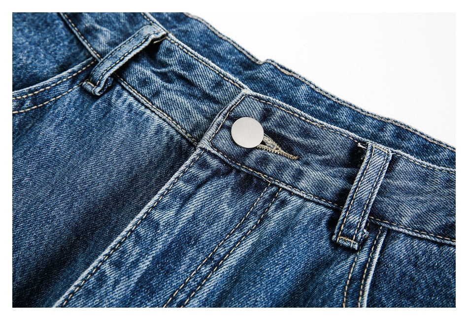 Close-up of blue washed jeans at the waistband, with a metal button, belt loops, and front fly stitching.