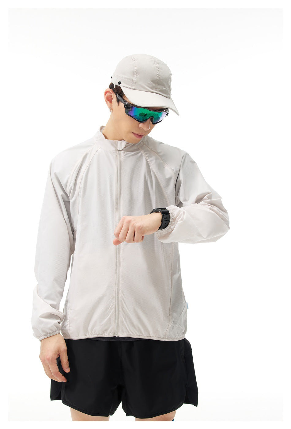 Model wearing a light gray full-zip jacket with a stand collar and elastic cuffs, checking a wristwatch.