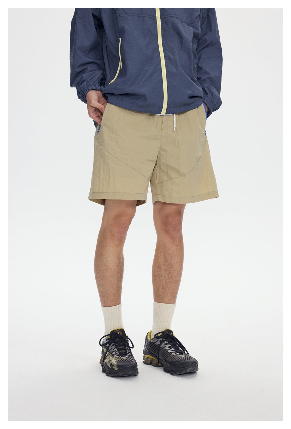 Close view of beige shorts with a drawstring waist, worn with a navy jacket.