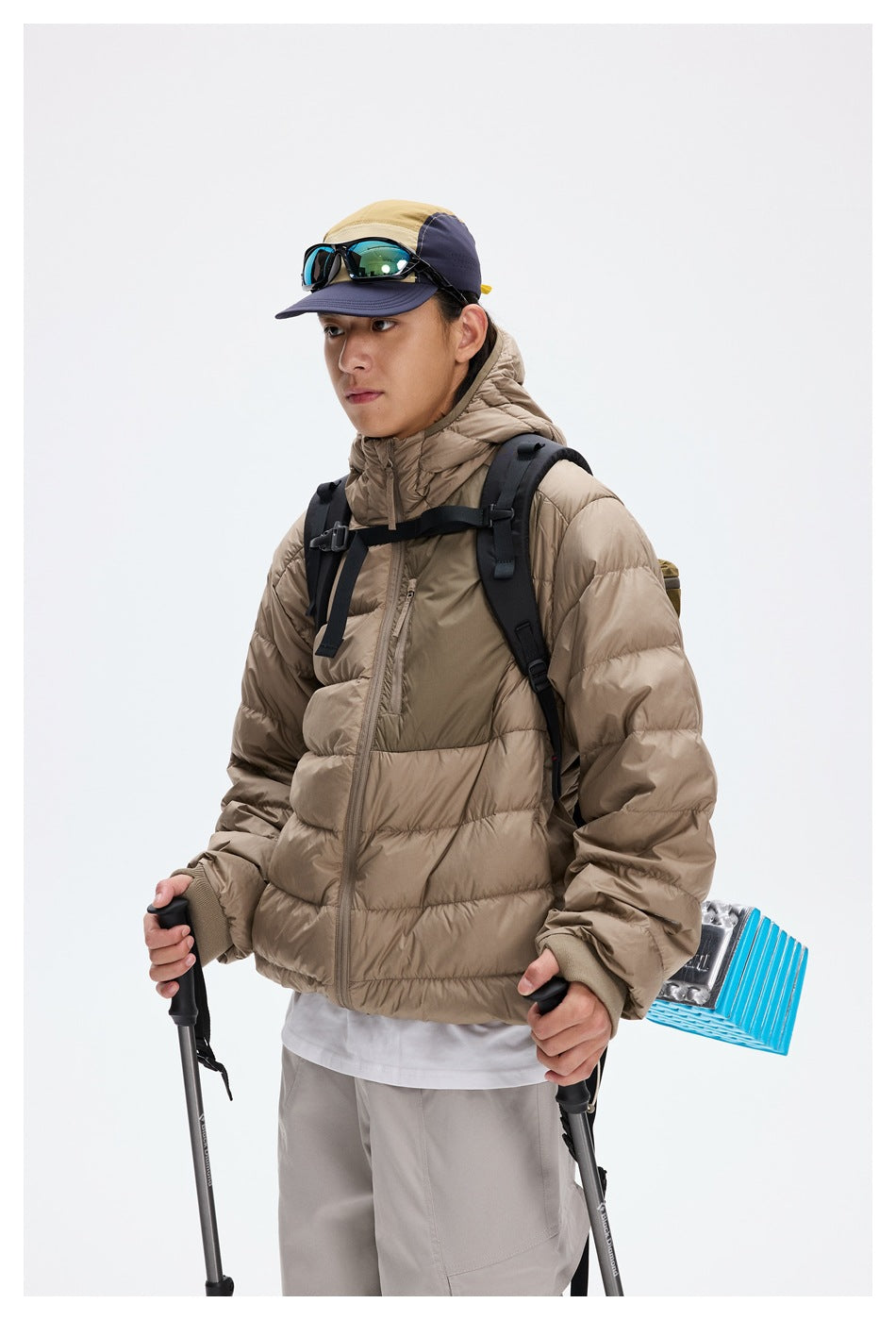 Close view of a model wearing a taupe hooded puffer jacket, shown from the front with a backpack.