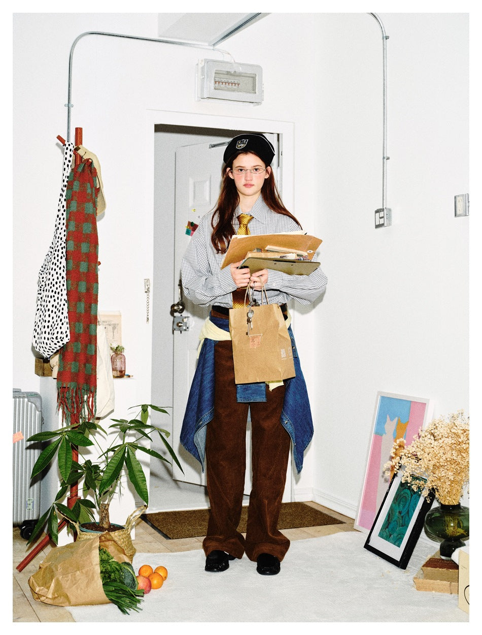 Model wearing a gray gingham shirt with a gold tie, beret, denim tied at the waist and brown corduroy pants