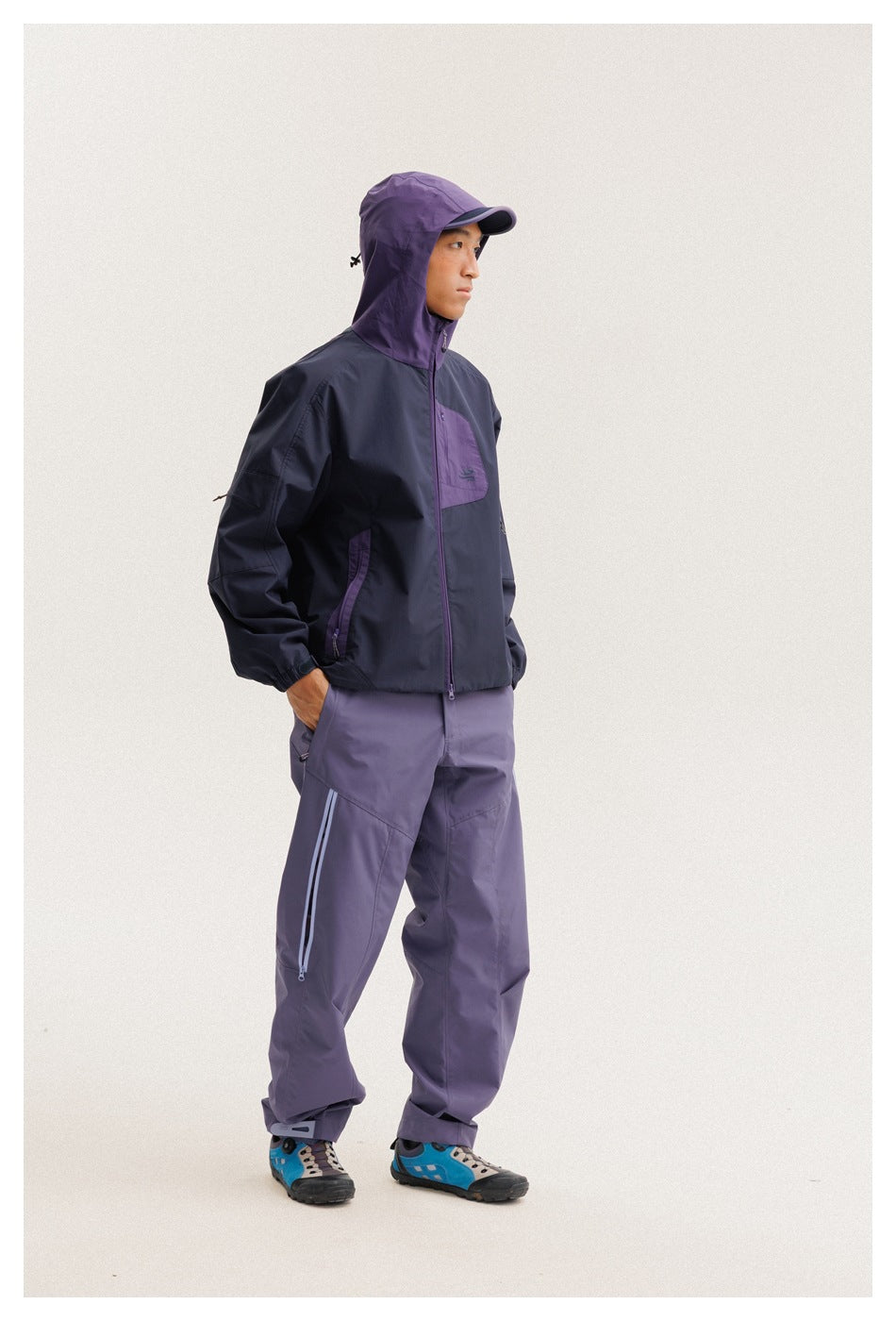 Model in a navy and purple hooded jacket with matching purple trousers, shown in side profile.
