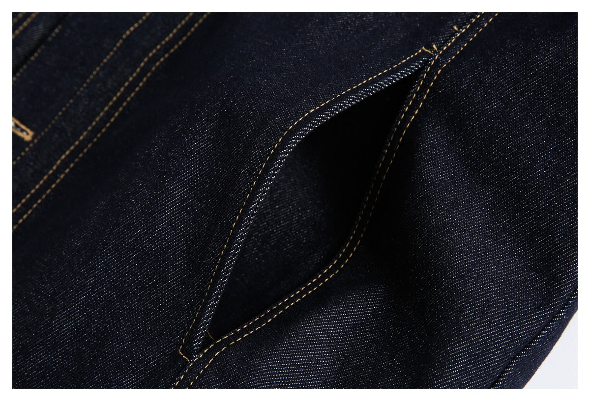 Close-up of a pocket opening on dark indigo denim, edged with gold stitching.