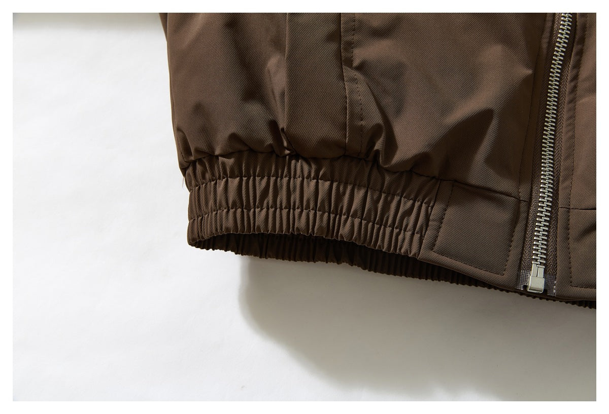 Close-up of a brown jacket hem with gathered elastic trim and a metal zipper.