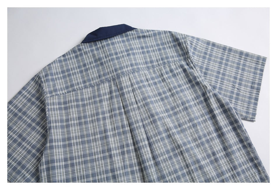 Back view of a blue-gray plaid short-sleeve shirt with a dark navy collar and center pleat.