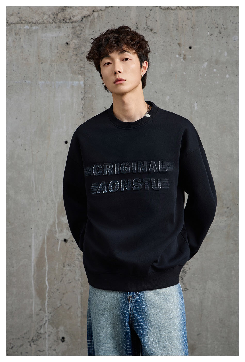 Close view of a model wearing a black crewneck sweatshirt with raised lettering and light blue jeans.