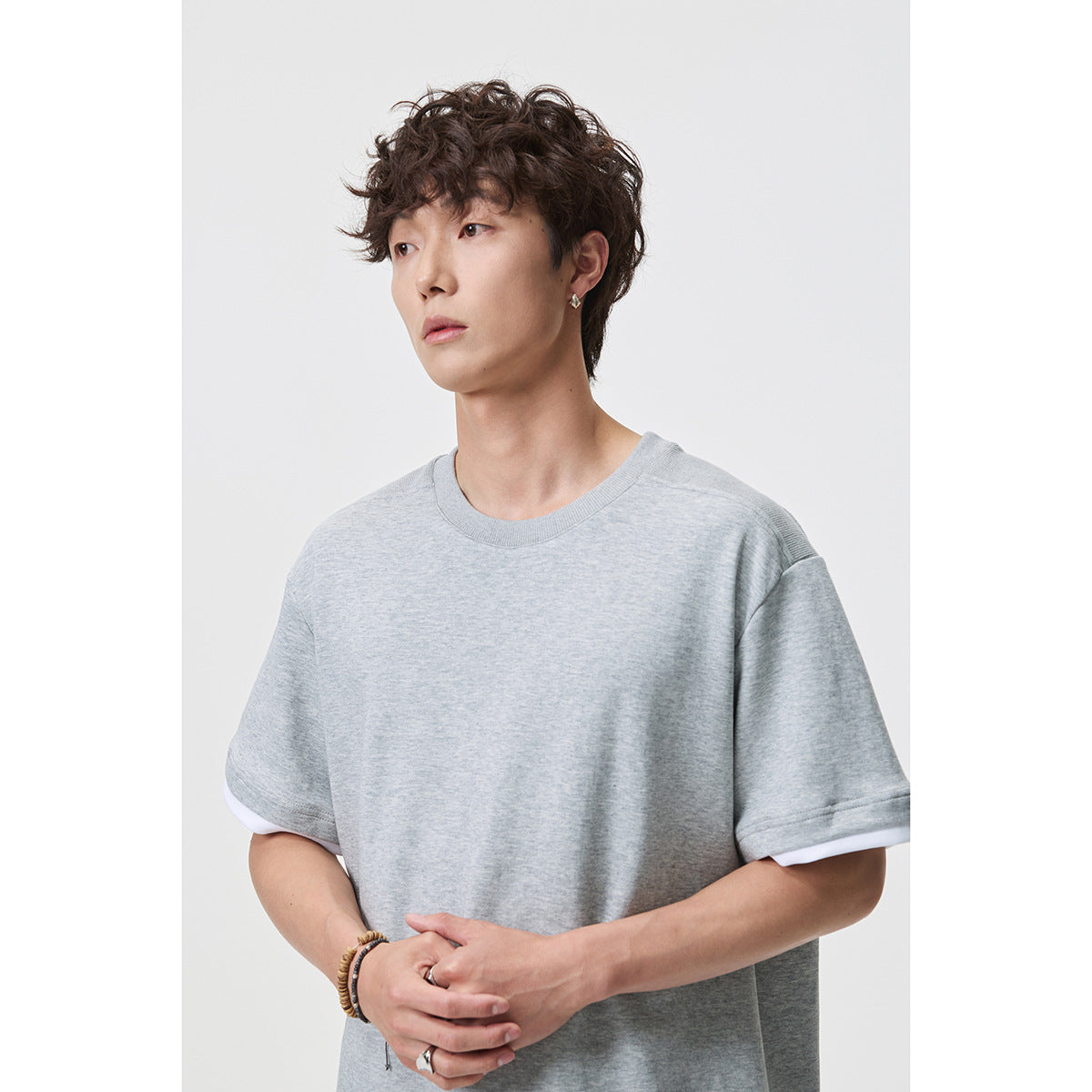 Model wearing a light gray oversized crew-neck T-shirt with white sleeve layers, shown from the front.