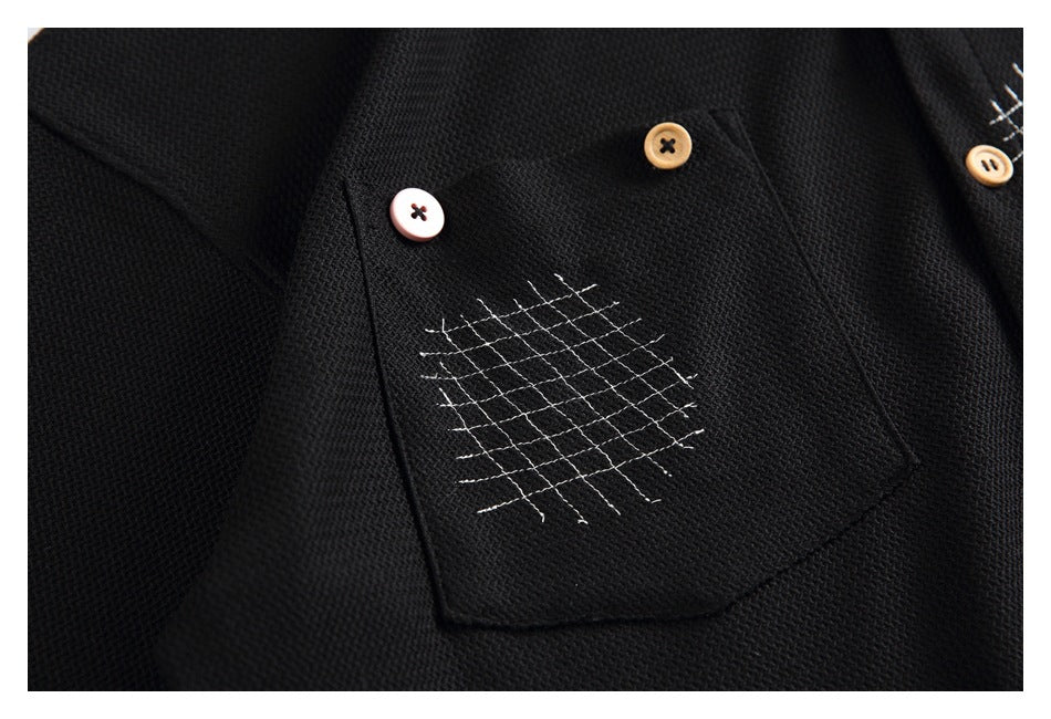 Close-up of a black shirt pocket with white grid stitching and contrasting decorative buttons.