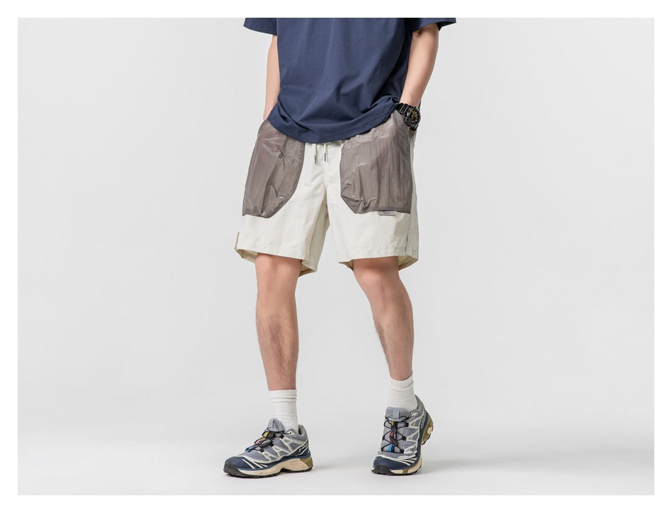 Cropped model wearing cream shorts with large gray patch pockets and a navy T-shirt, front view with hands in pockets.