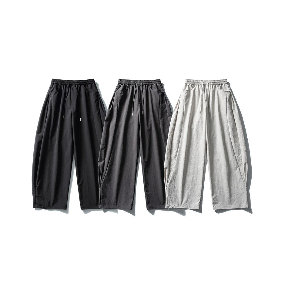 Three pairs of relaxed, wide-leg drawstring pants shown from the front in black, charcoal gray, and light gray.