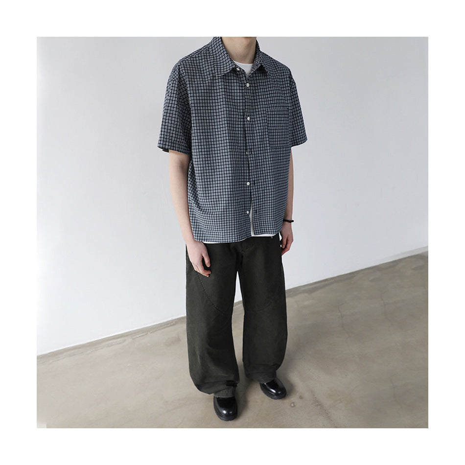 Cropped view of model in plaid short-sleeve shirt over a white tee with dark wide-leg pants and black shoes