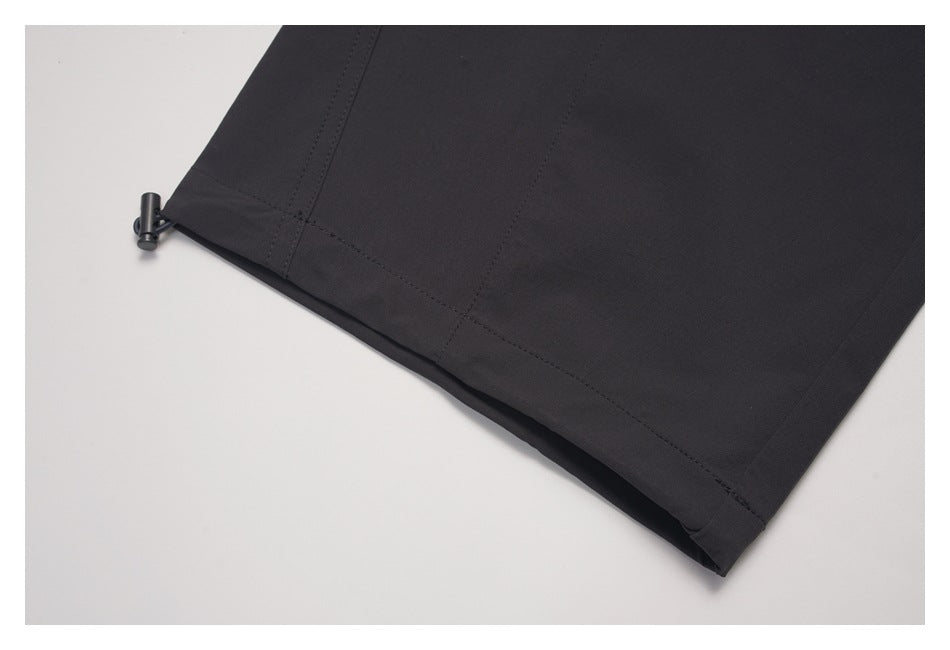 Close-up of a black garment hem with a small cord toggle and stitched seams.