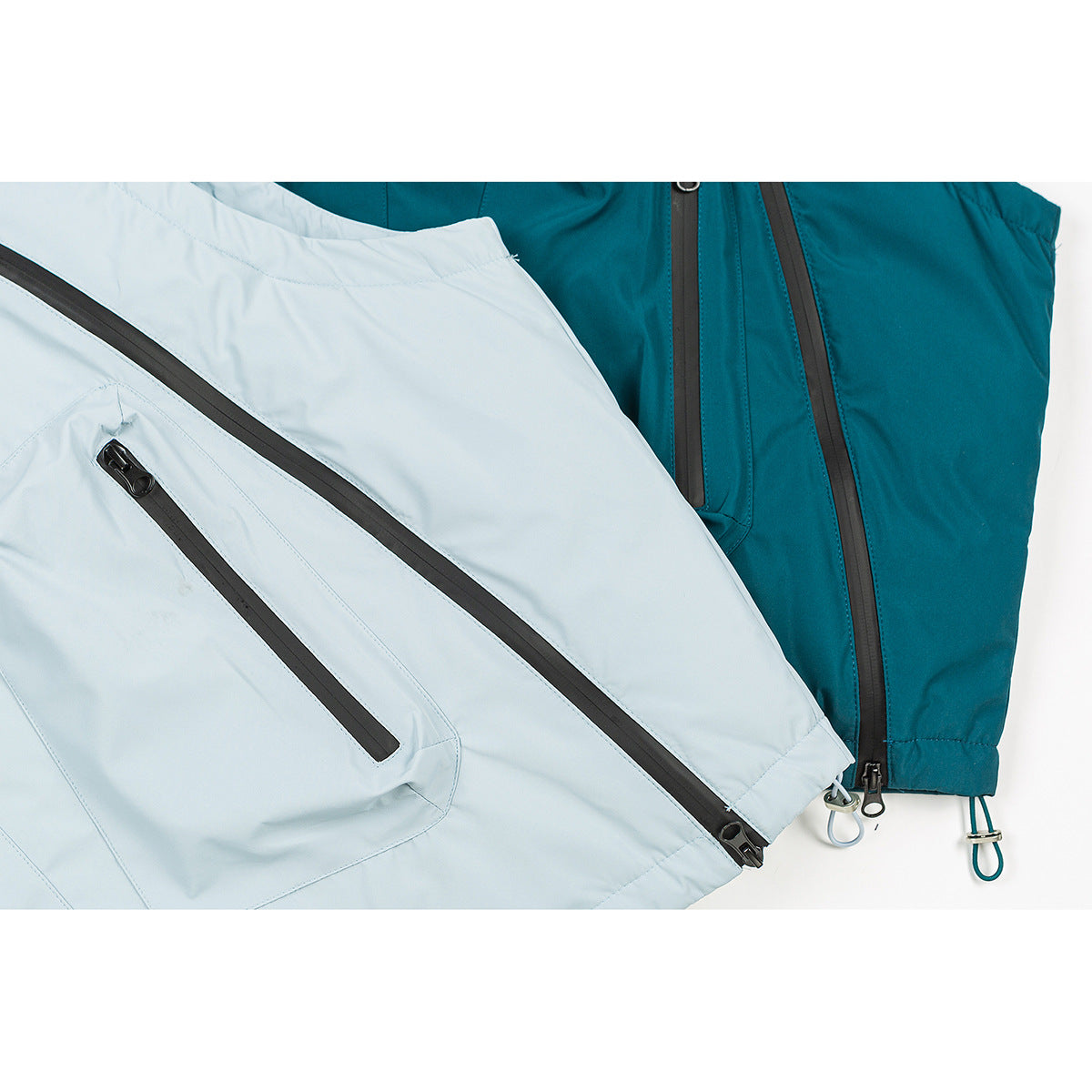 Close-up of pale blue and teal hooded vests with black zippers and zip pockets.