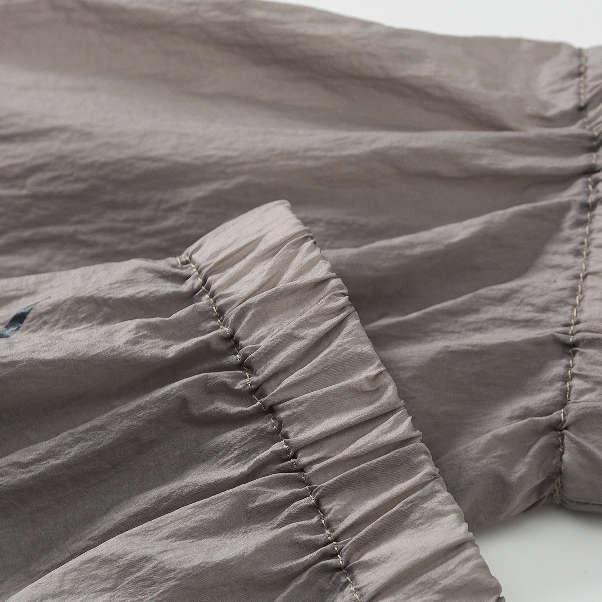 Close-up of gathered stitching and a curved seam on crinkled taupe-gray fabric.