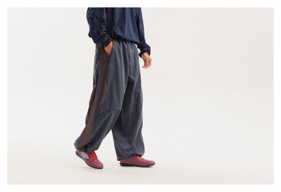 Cropped model wearing loose charcoal trousers with brown side panels, shown from a rear three-quarter angle.