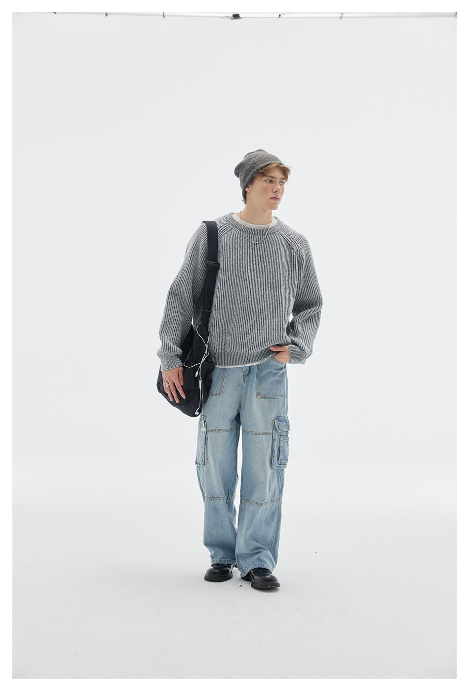 Model wearing a light gray rib-knit crew-neck sweater with light jeans, a gray beanie and a dark shoulder bag