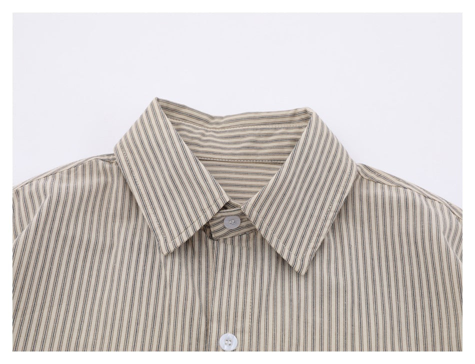 Close-up of the pointed collar and top button on a light beige shirt with fine dark stripes.