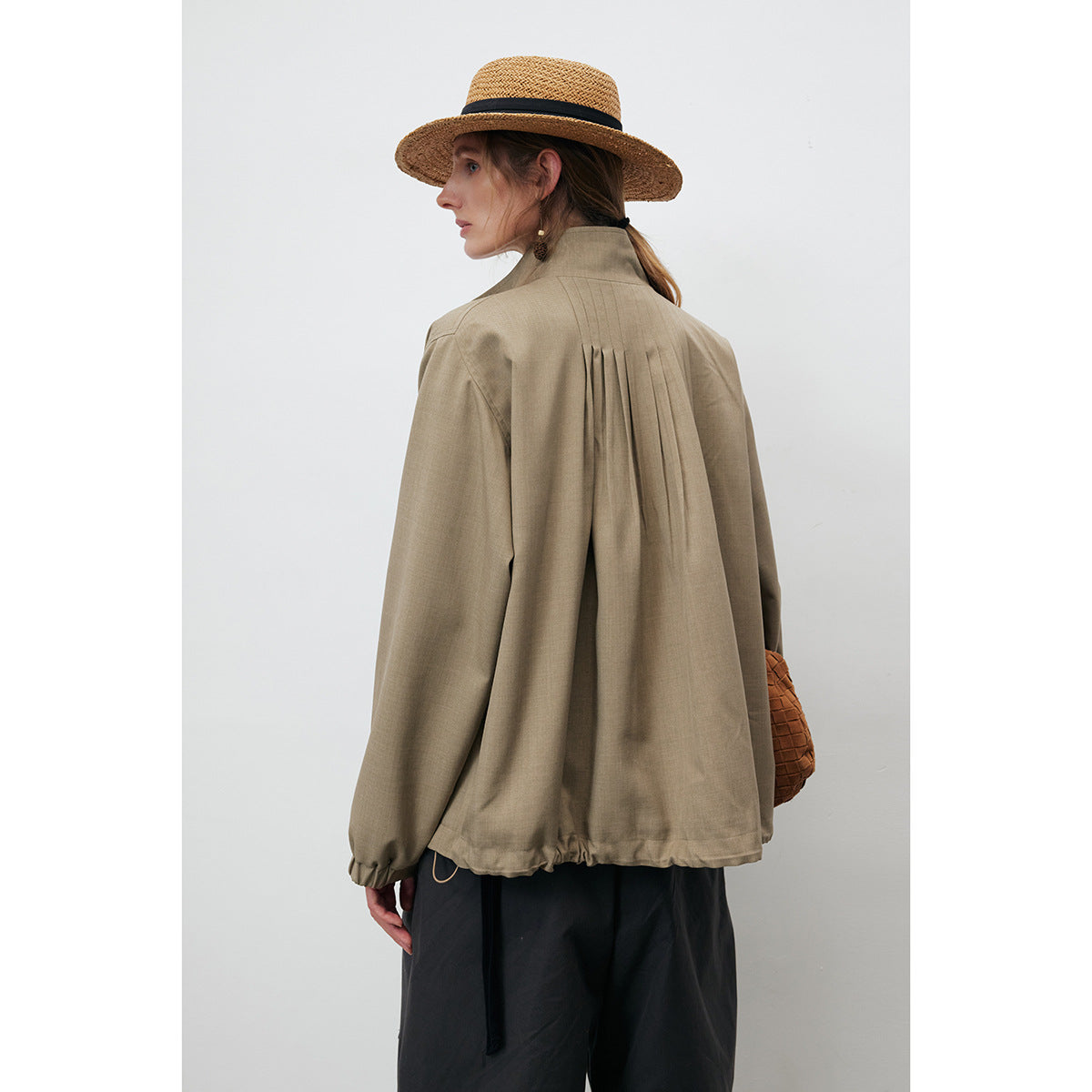Model shown from behind in a taupe jacket with vertical back pleats and an elasticized hem.