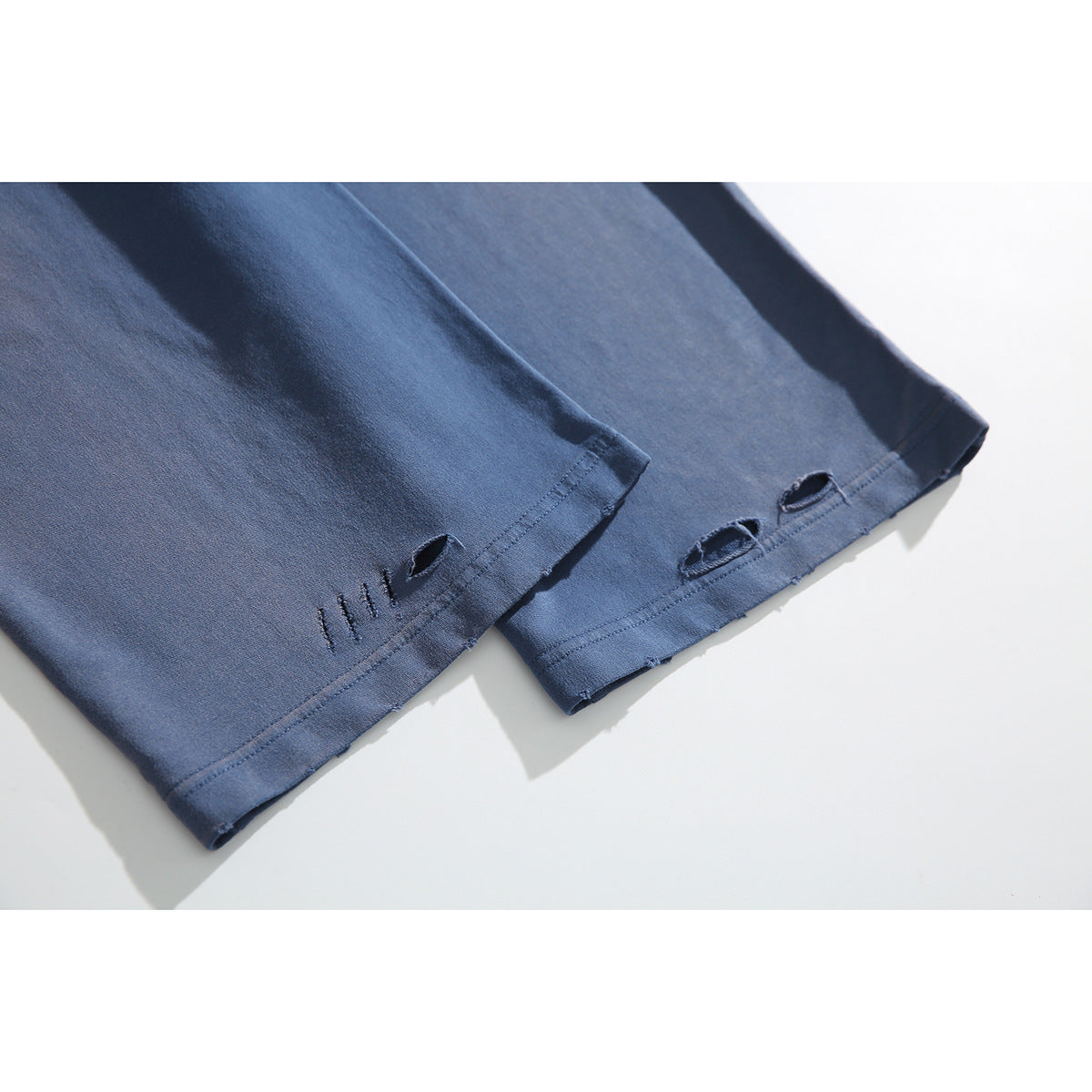 Close-up of slate-blue pant legs showing stitched hems and small distressed openings.