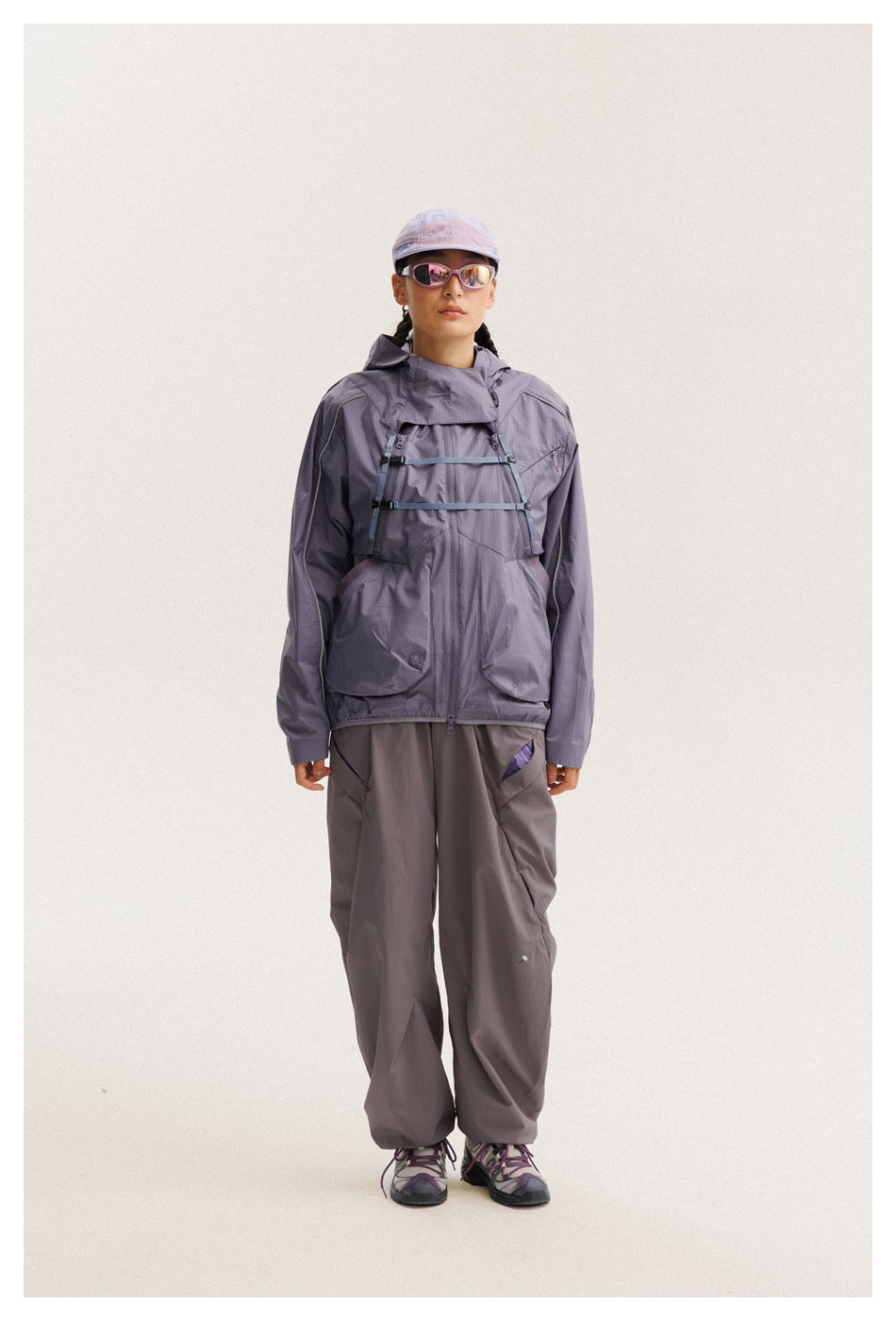 Model wearing a lavender-gray hooded jacket with chest straps and large pockets, paired with loose dark-gray pants.