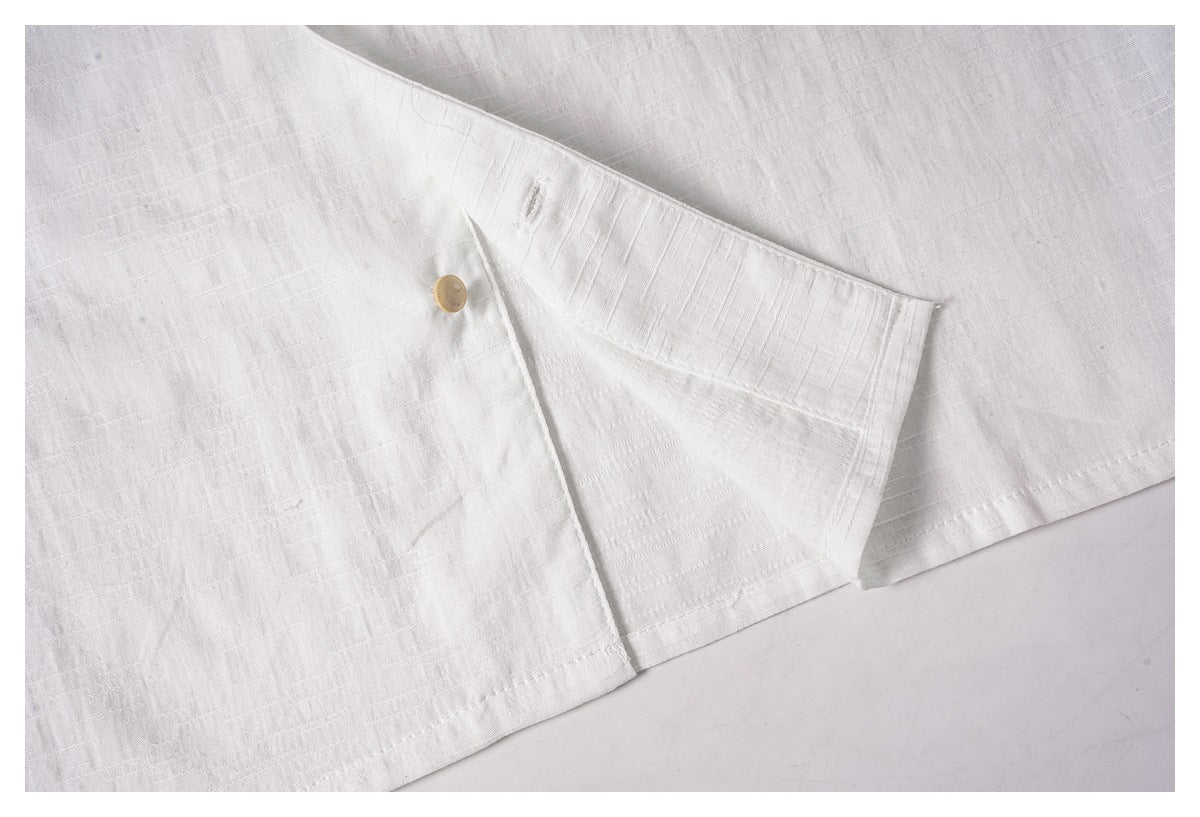 Close-up of the white shirt's lower hem and side opening with a tan button.