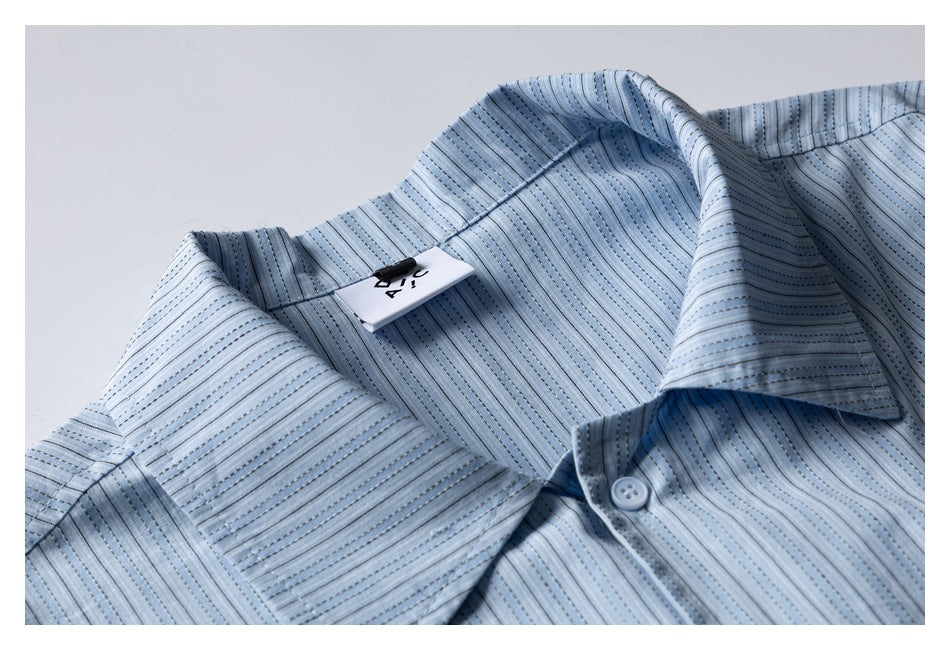 Close-up of a pale blue striped short-sleeve shirt collar, placket button, and attached neck tag.