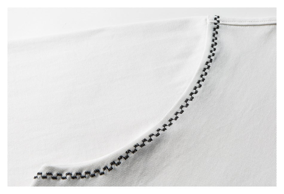 Close-up of a curved garment seam finished with dark contrasting stitching on white fabric.