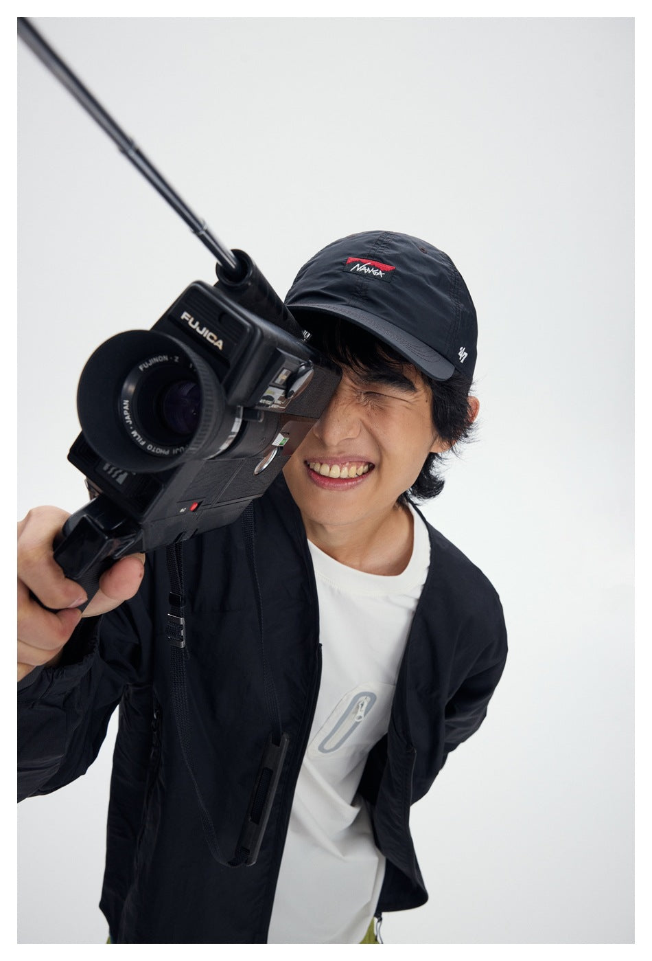 Close view of a model in a black jacket over a white graphic T-shirt, holding a video camera.