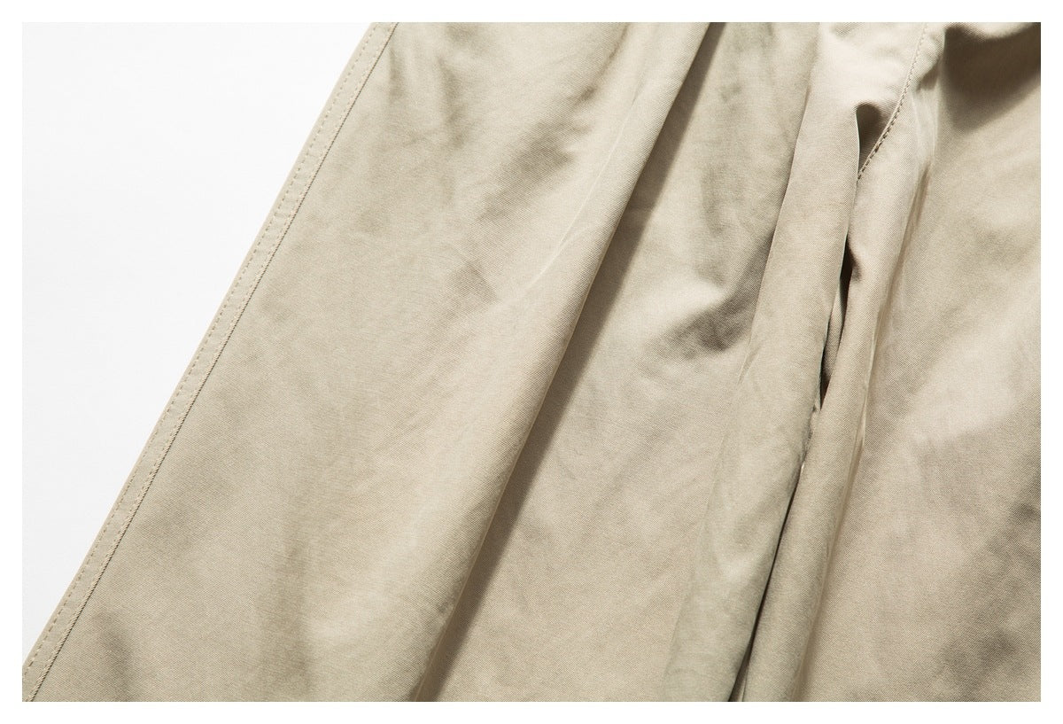 Close-up of light beige pants fabric with a stitched seam and part of a pocket opening.