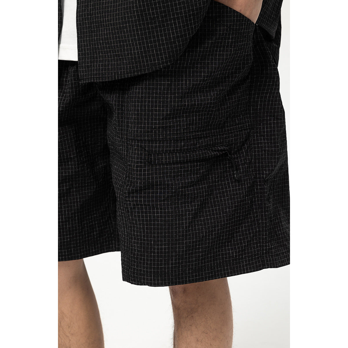 Close-up of black windowpane-check shorts worn on a person, showing a flap pocket at the side.