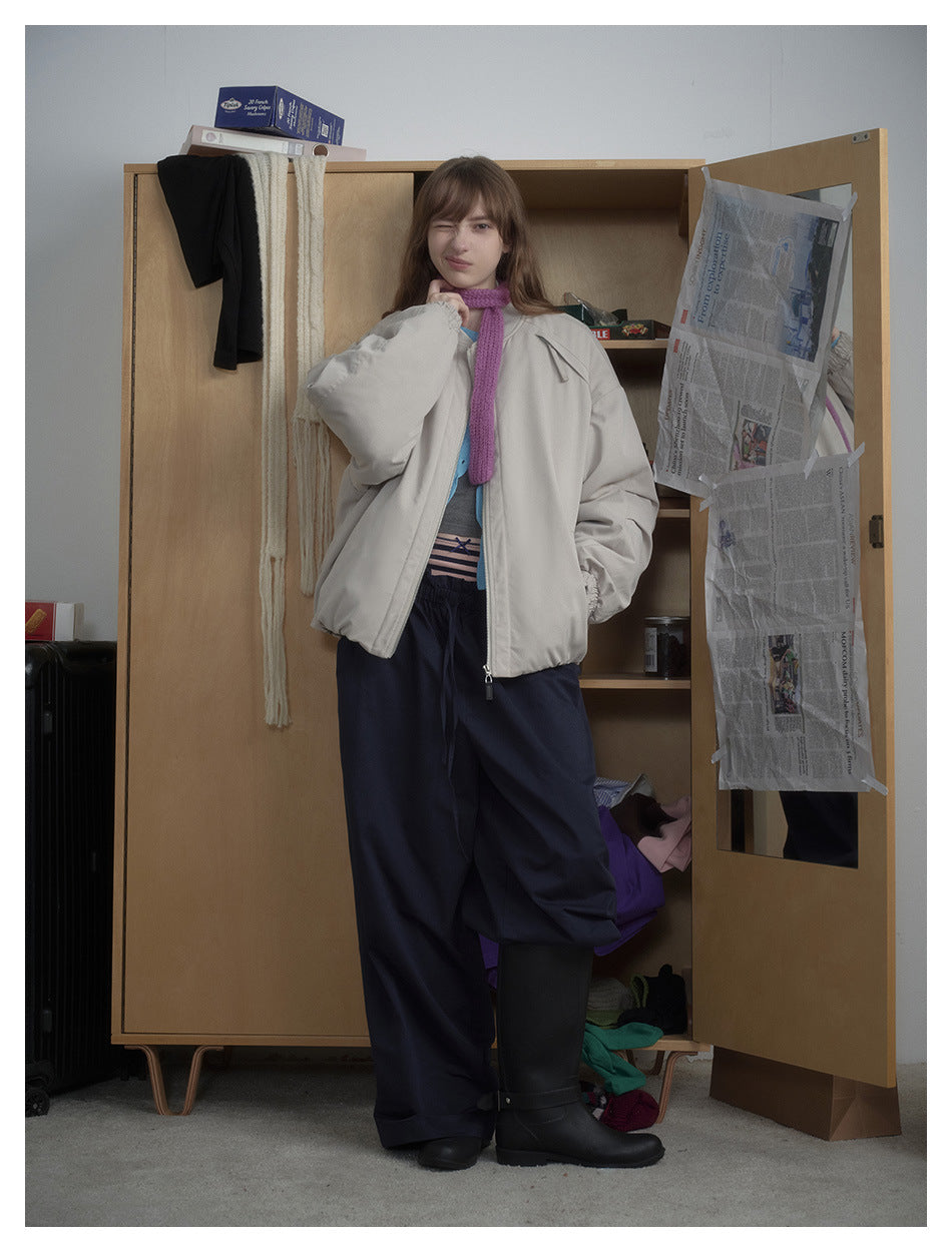 Model poses in a light beige-gray oversized zip jacket, navy trousers, and a purple scarf.