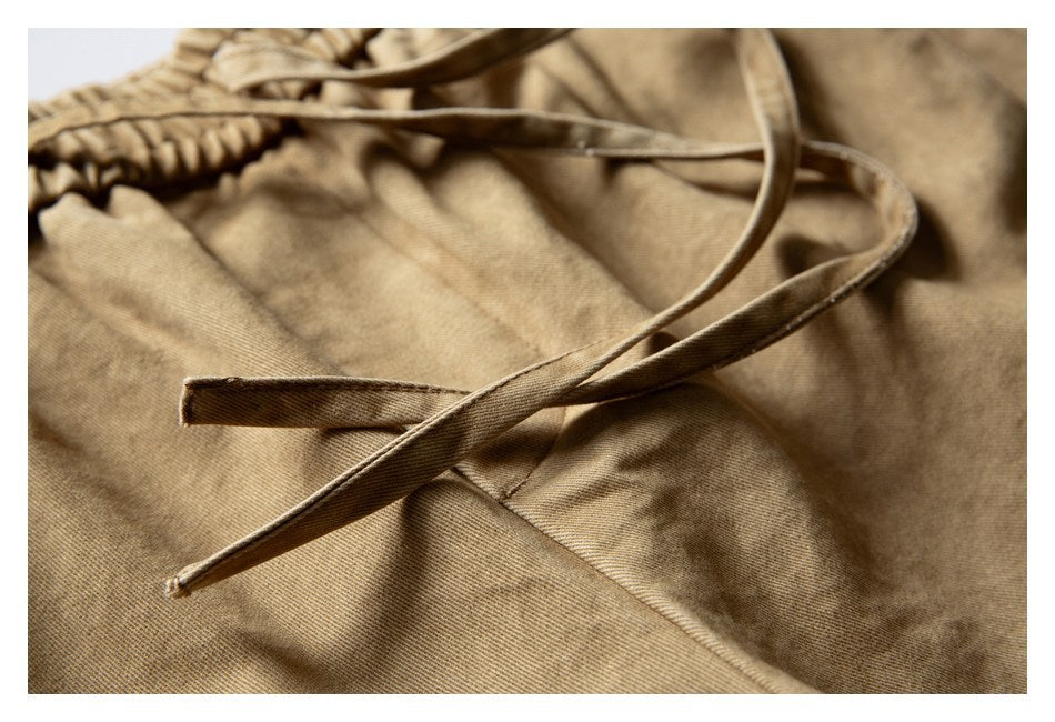 Close-up of tan shorts showing the elastic waist and long adjustable drawstrings.