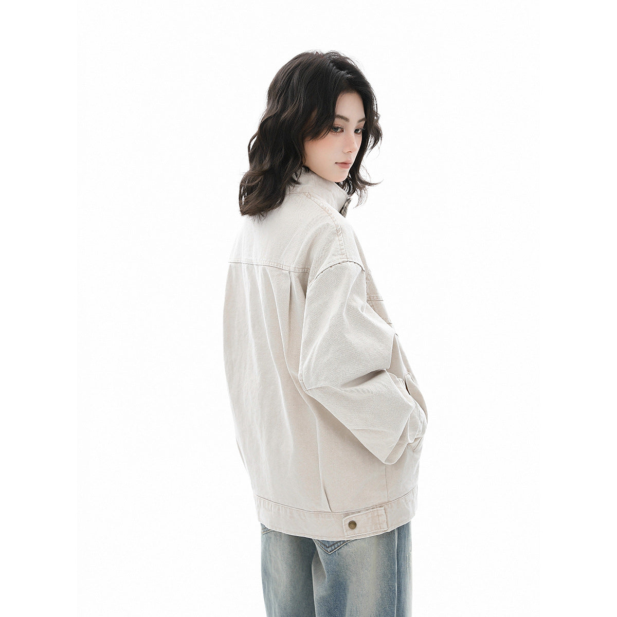 Side and back view of a model wearing a light beige jacket with a buttoned hem tab and blue jeans.