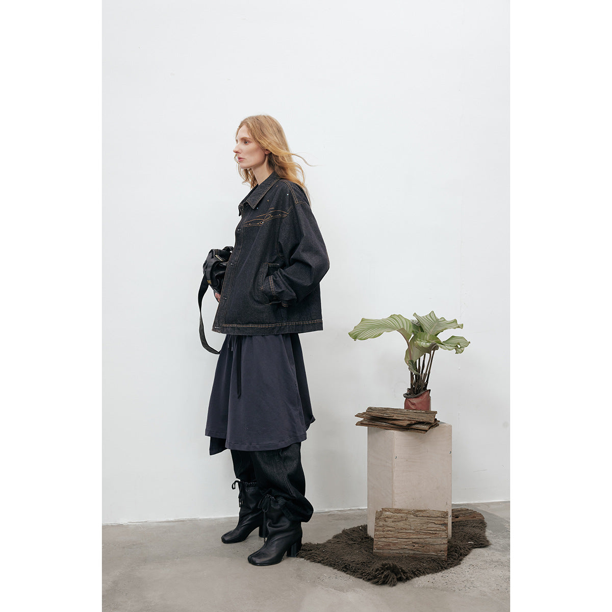 Side view of a model wearing an oversized black denim jacket with tan stitching and a pointed collar.