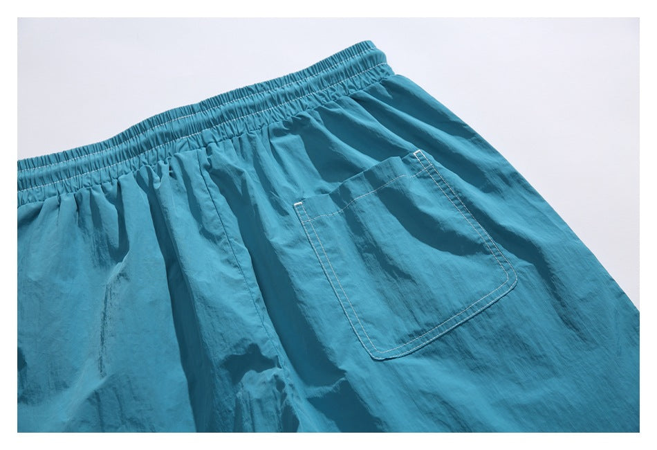 Teal shorts laid flat, showing the elastic waistband, white contrast stitching, and a large patch pocket.