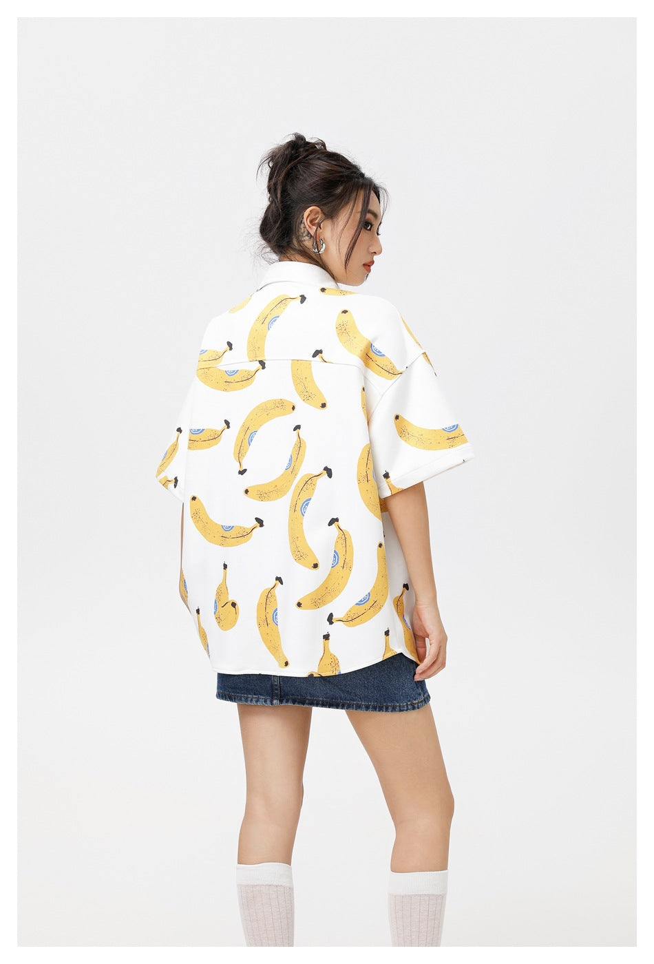 Rear view of a model wearing the white banana-print shirt with a denim mini skirt.
